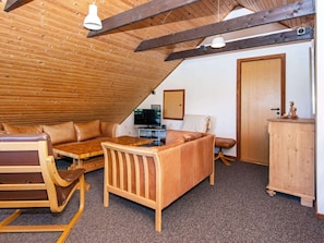 A cozy attic room with a wooden ceiling, a sofa, a wooden table, and a television. - 10 Person Holiday Home in Orsted (Ørsted)