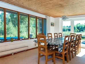 A dining area with a large table and chairs, large windows with a view of greenery, and a ceiling fan. - 10 Person Holiday Home in Orsted (Ørsted)