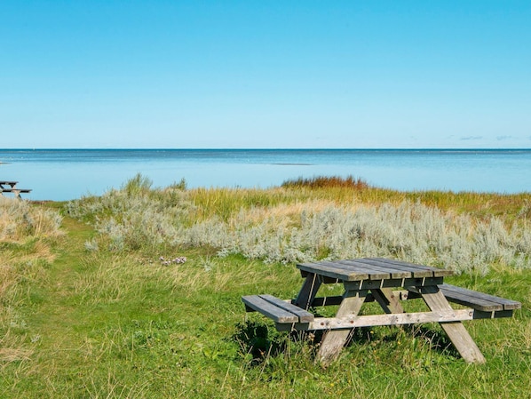 A wooden picnic table in a grassy area with a view of the water.