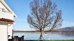 Ein Anwesen am Seeufer mit einer Holzterrasse, Sitzgelegenheiten im Freien und einem Schaukelstuhl.