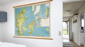 Une pièce avec une grande carte du Danemark accrochée au mur, un lit et un couloir qui mène à l’extérieur.