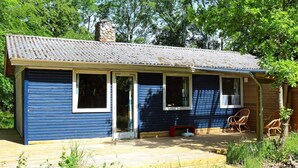 A small, single-story cabin with a blue exterior, a tiled roof, and a porch area with outdoor seating. - Rustic Holiday Home in Hadsund near Sea (Hadsund)