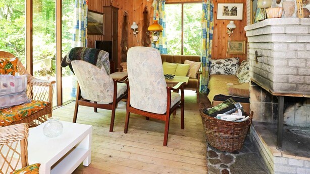 A cozy cabin interior with a stone fireplace, wooden furniture, and a view of the forest. - Rustic Holiday Home in Hadsund near Sea (Hadsund)