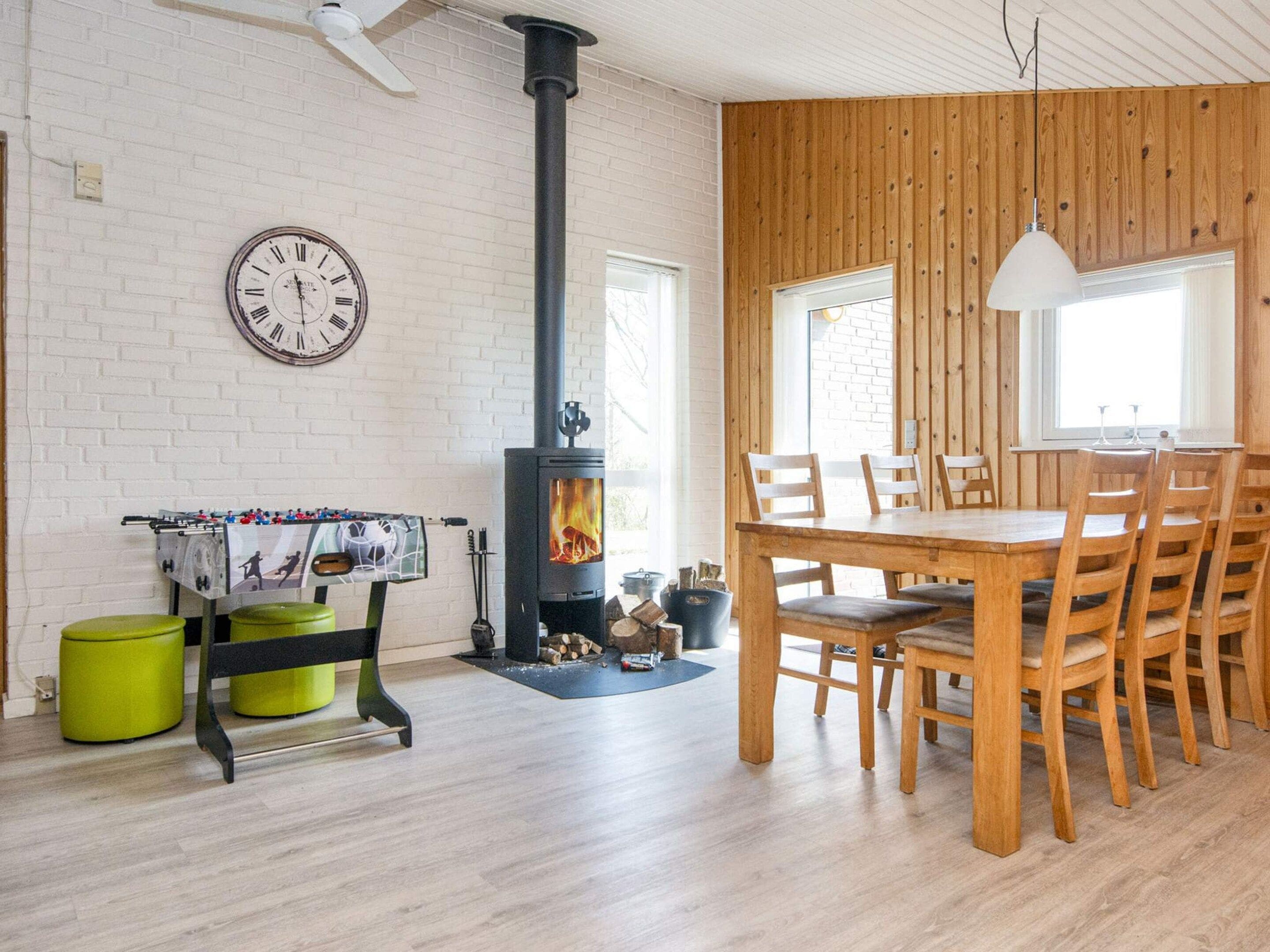 Una habitación con chimenea, una mesa de comedor con sillas, un reloj en la pared y una ventana.