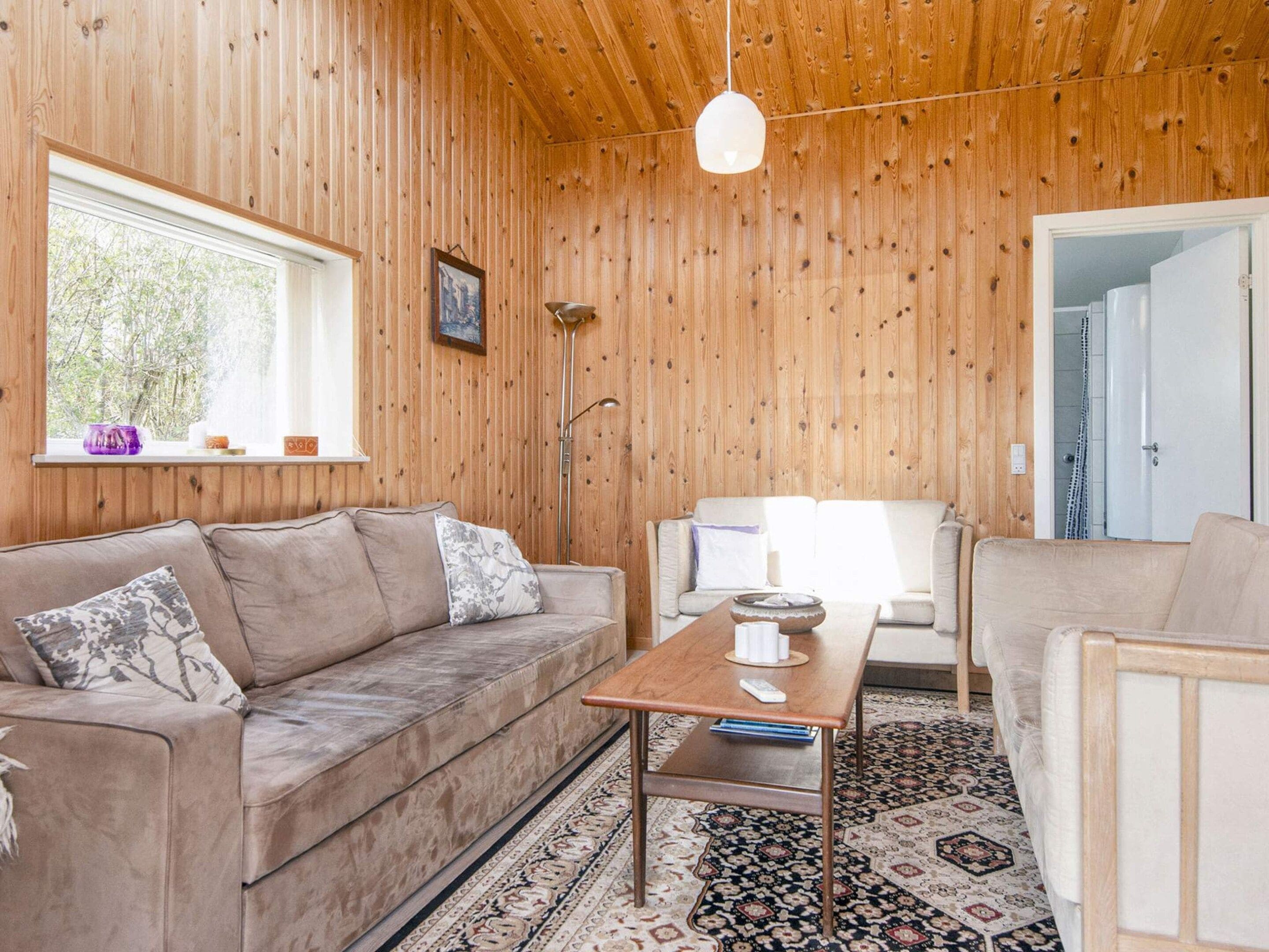 A cozy room with a wooden ceiling, a sofa, a coffee table, and a patterned rug.