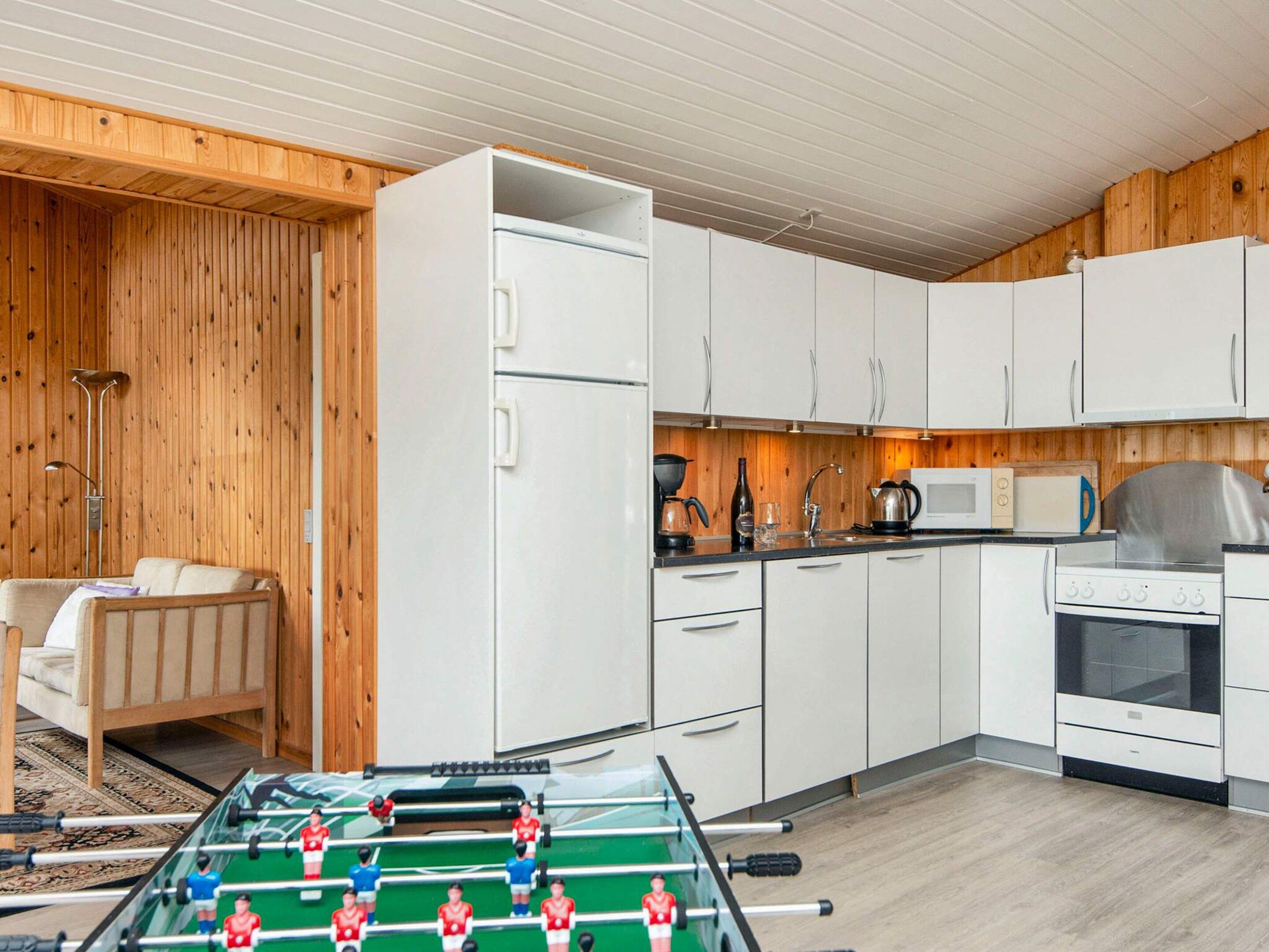 Cozinha compacta com armários brancos, fogão, micro-ondas e mesa de futebol.