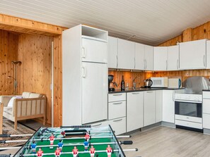 Cocina compacta con armarios blancos, estufa, microondas y mesa de fútbol.