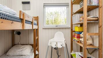 Ein Schlafzimmer mit Etagenbetten, einem weißen Stuhl, einem Fenster und Holzregalen mit Büchern und Spielzeug.