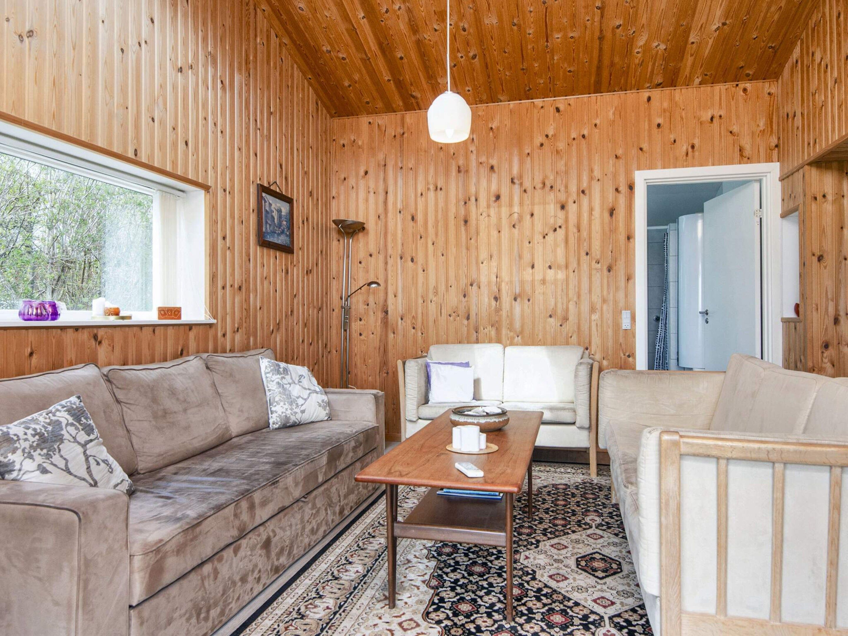 A cozy room with a wooden ceiling, a sofa, a chair, a small table, and a patterned rug.