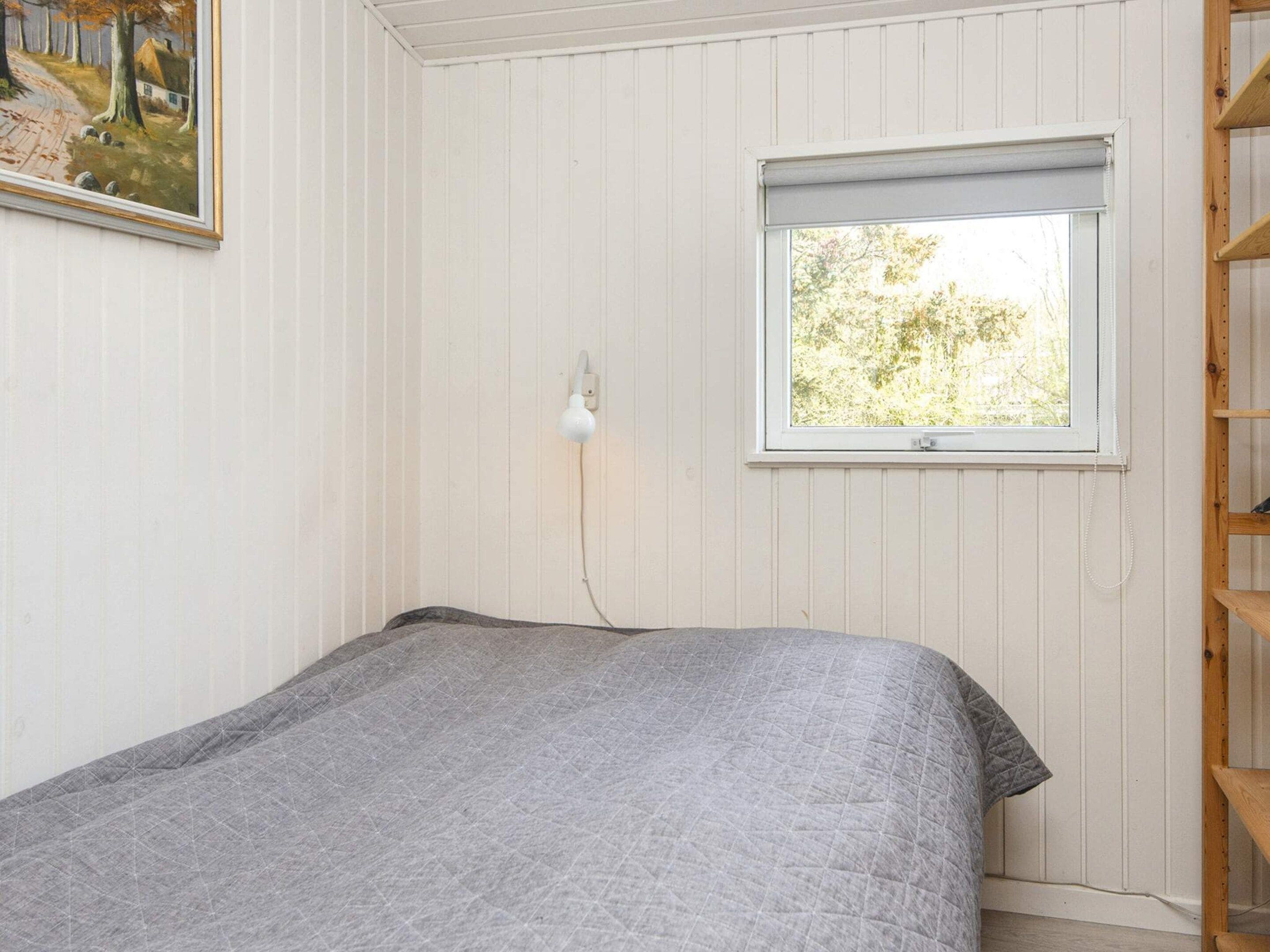 Una habitación con cama, ventana con vista a árboles y un cuadro en la pared.