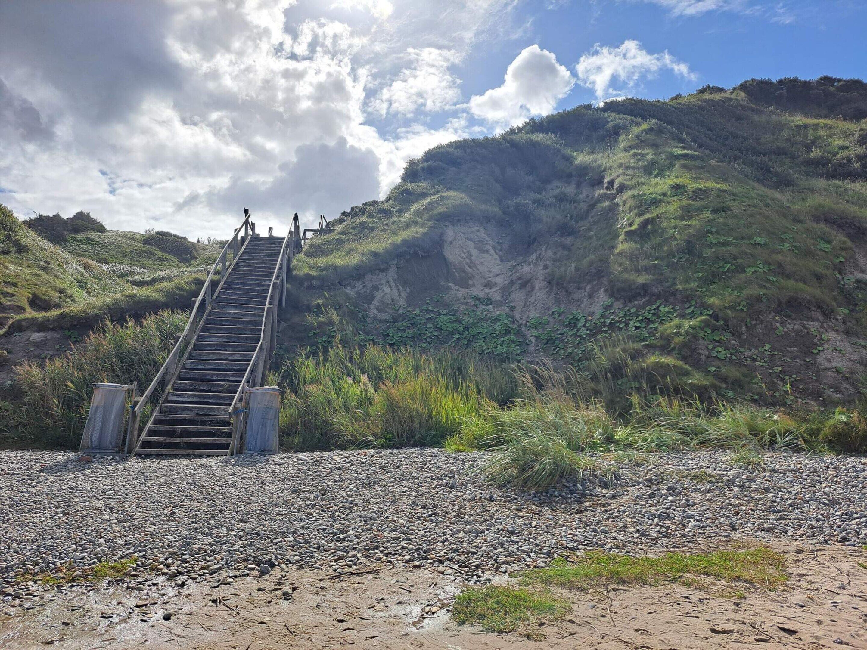 A wooden staircase leading up a hill with a rocky foreground and a grassy hillside in the background.