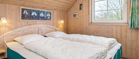 A wooden cabin bedroom with a bed, a window, and a wall-mounted picture.