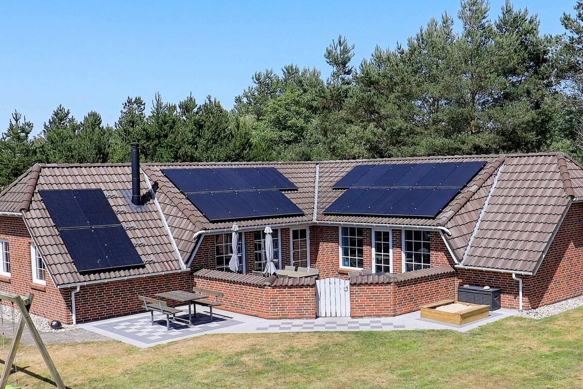 A two-story brick house with solar panels on the roof, a patio with a table and chairs, and a swing set in the yard.