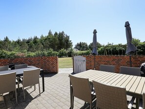 An outdoor patio area with brick walls, a wooden table, wicker chairs, and a grill. - 4 Star Holiday Home in Oksbol (Oksbol)