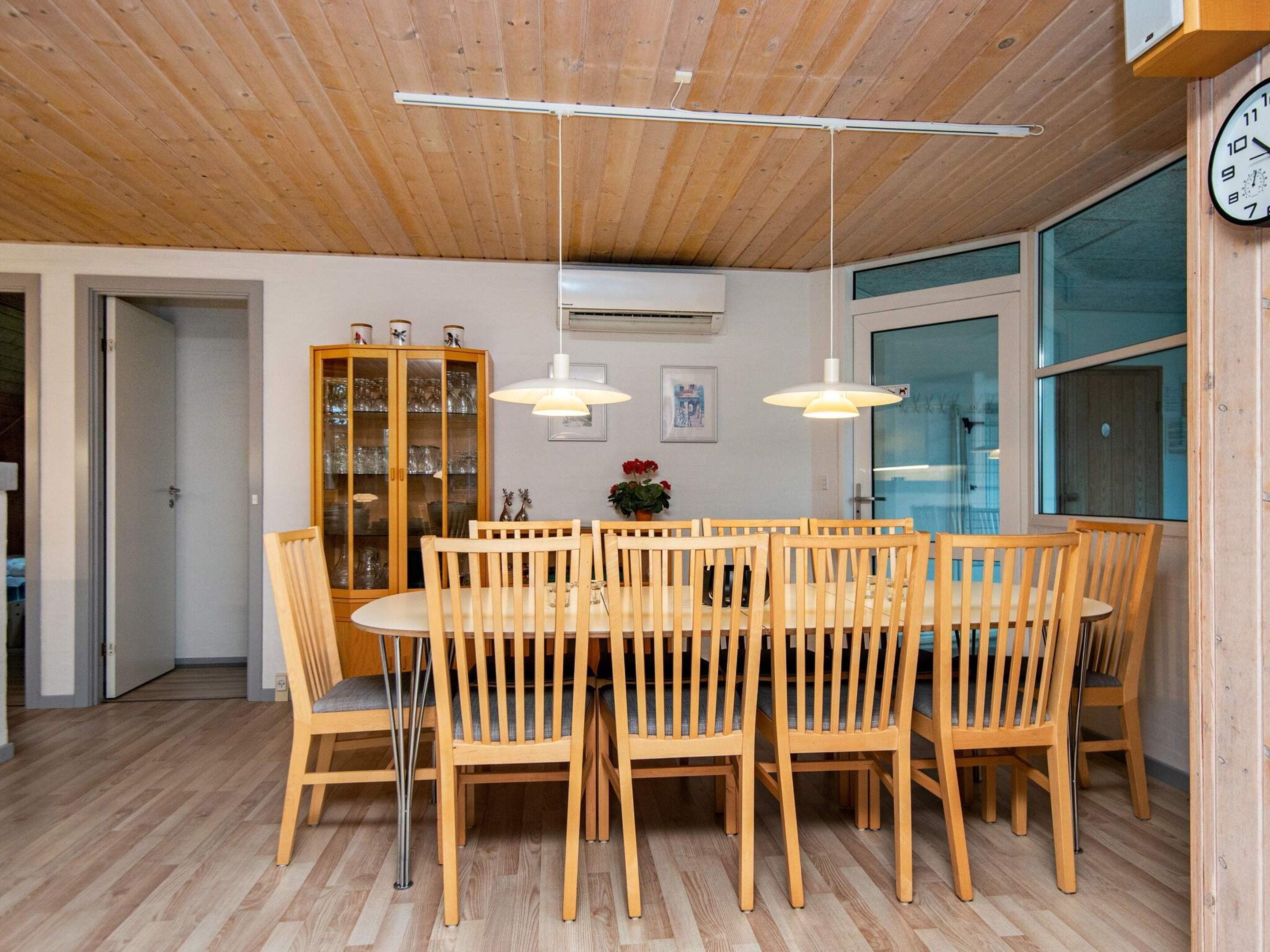 Et spiseområde med et træbord og stole, et skab med glasdøre samt et ur på væggen.