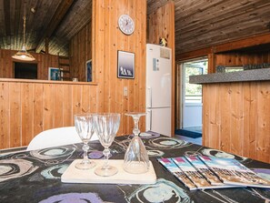 A wooden interior with a table set for dining, a clock, and a refrigerator.