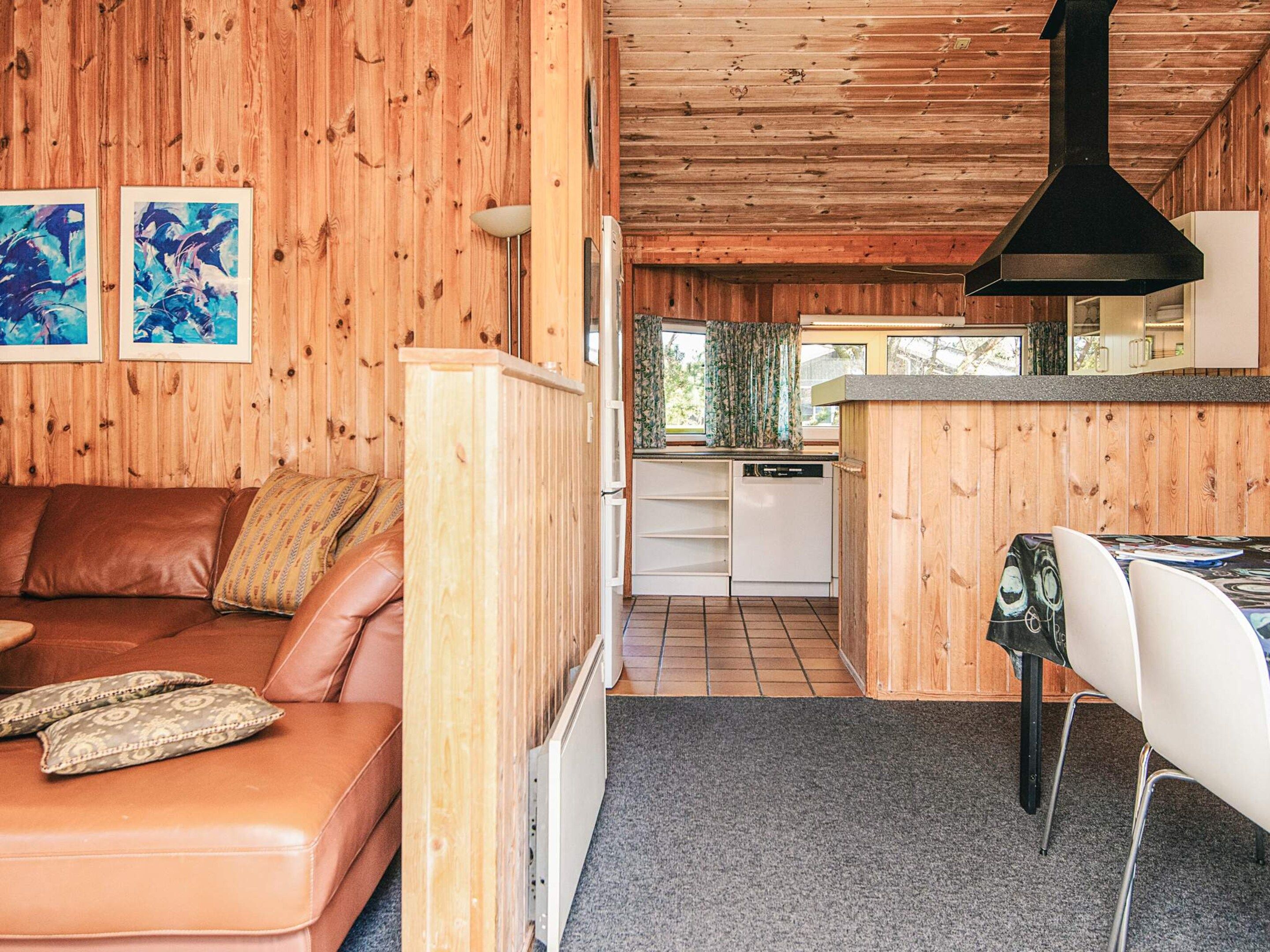 A cozy cabin interior with a wooden interior, a living area with a sofa and cushions, a dining area with a table and chairs, and a kitchen with a dishwasher.