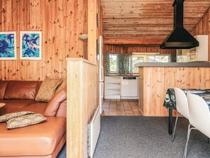 A cozy cabin interior with a wooden interior, a living area with a sofa and cushions, a dining area with a table and chairs, and a kitchen with a dishwasher.