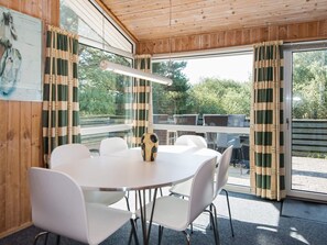 A room with a round table and white chairs, wooden walls, and large windows with curtains. - 6 Person Holiday Home in Fano (Fano)