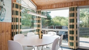 A dining area with a round table and white chairs, wooden ceiling, and large windows with curtains. - 6 Person Holiday Home in Fano (Fano)