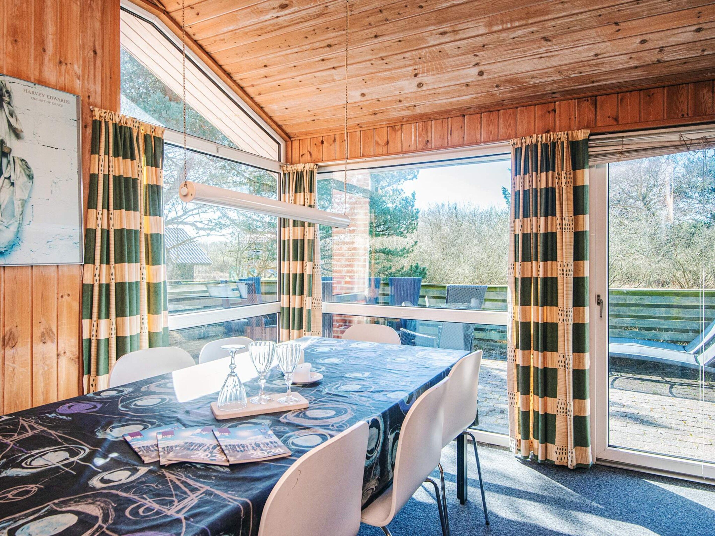 A wooden interior with a table set for dining, large windows, and a view of the outdoors.