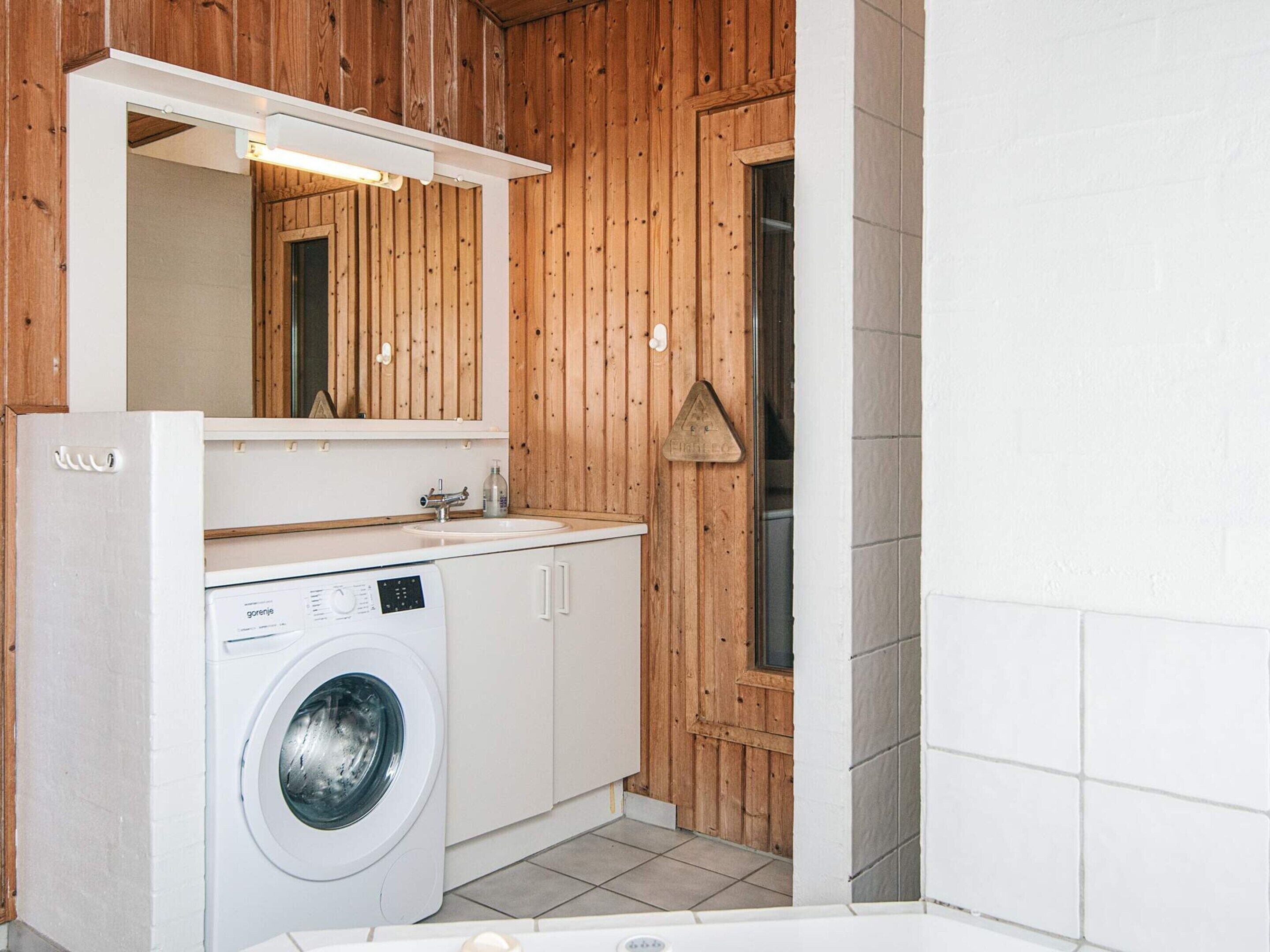 A compact bathroom with a washing machine, a sink, and a mirror.