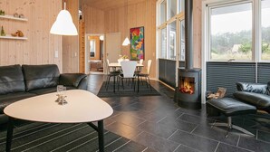 Un salón espacioso con chimenea, paredes de madera, una zona de comedor y ventanas amplias.