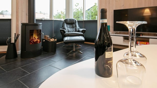 Un salón moderno con una estufa de leña, un sillón de cuero, una botella de vino y un vaso sobre una mesa blanca.