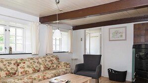 Un salon chaleureux avec un canapé à motifs floraux, un fauteuil sombre, une table basse en bois et une cheminée.