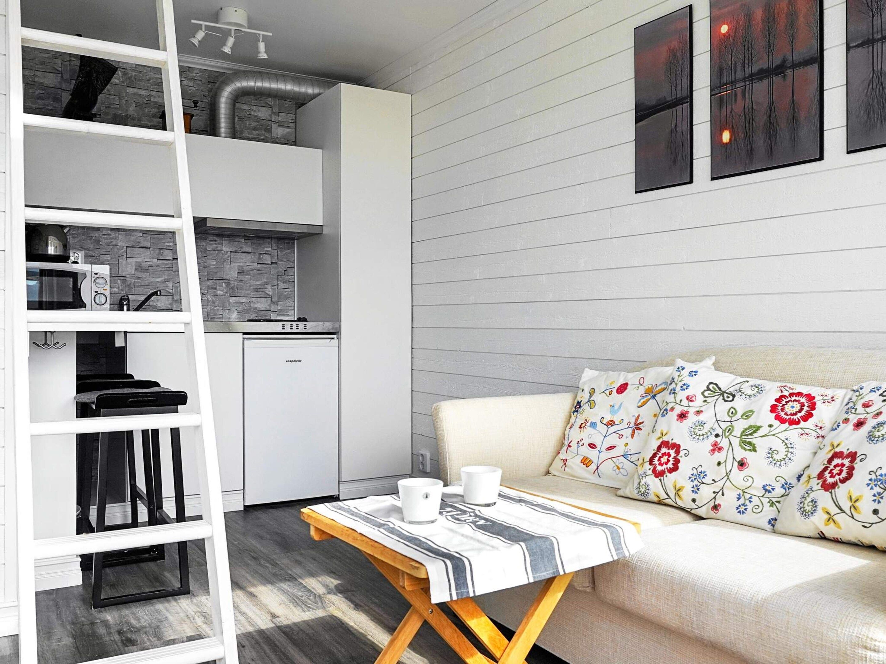 A compact living space with a kitchenette, a sofa with floral cushions, and a small table with a cup.