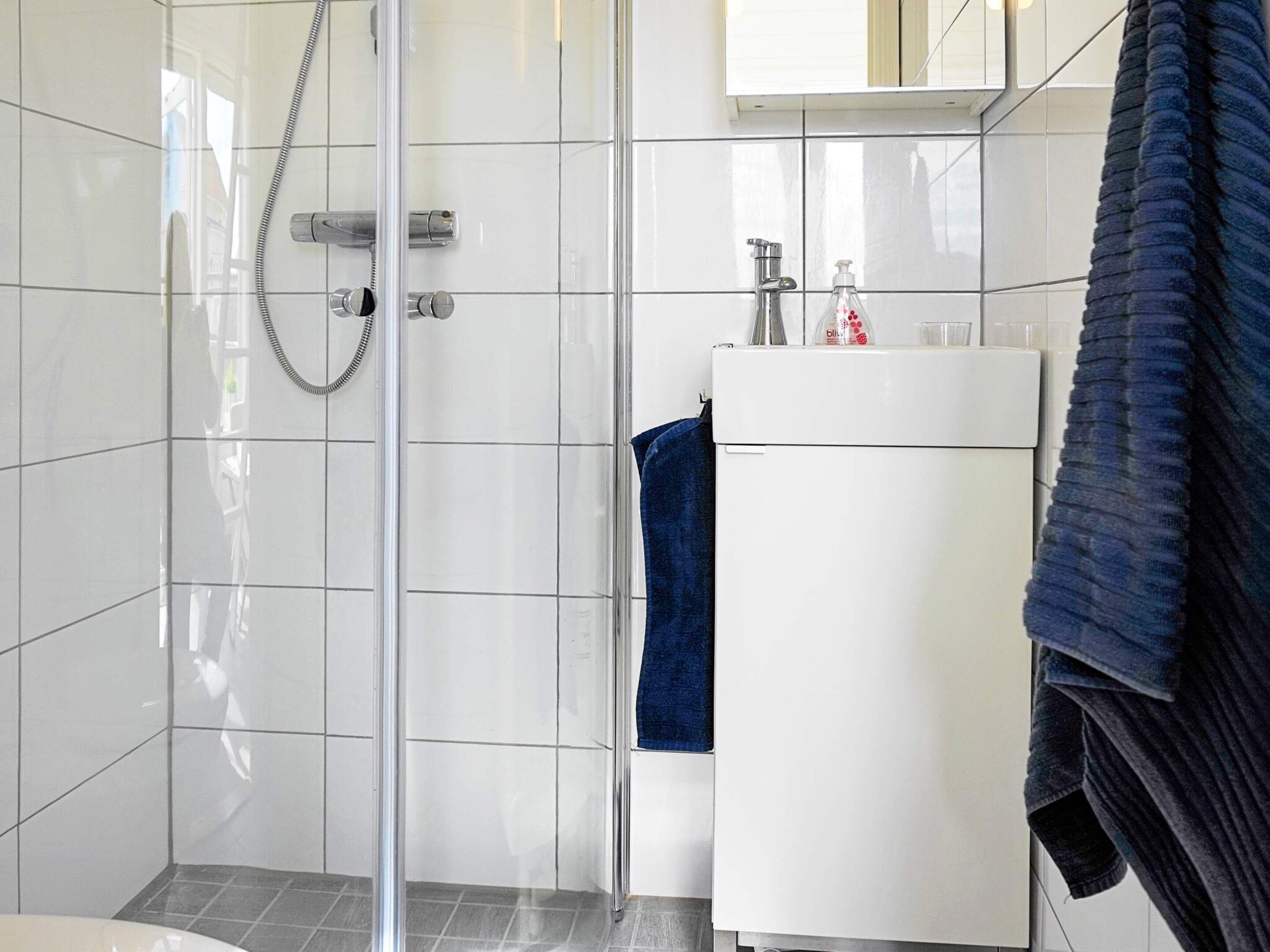 A bathroom with a glass-enclosed shower, a white sink, and a towel rack.