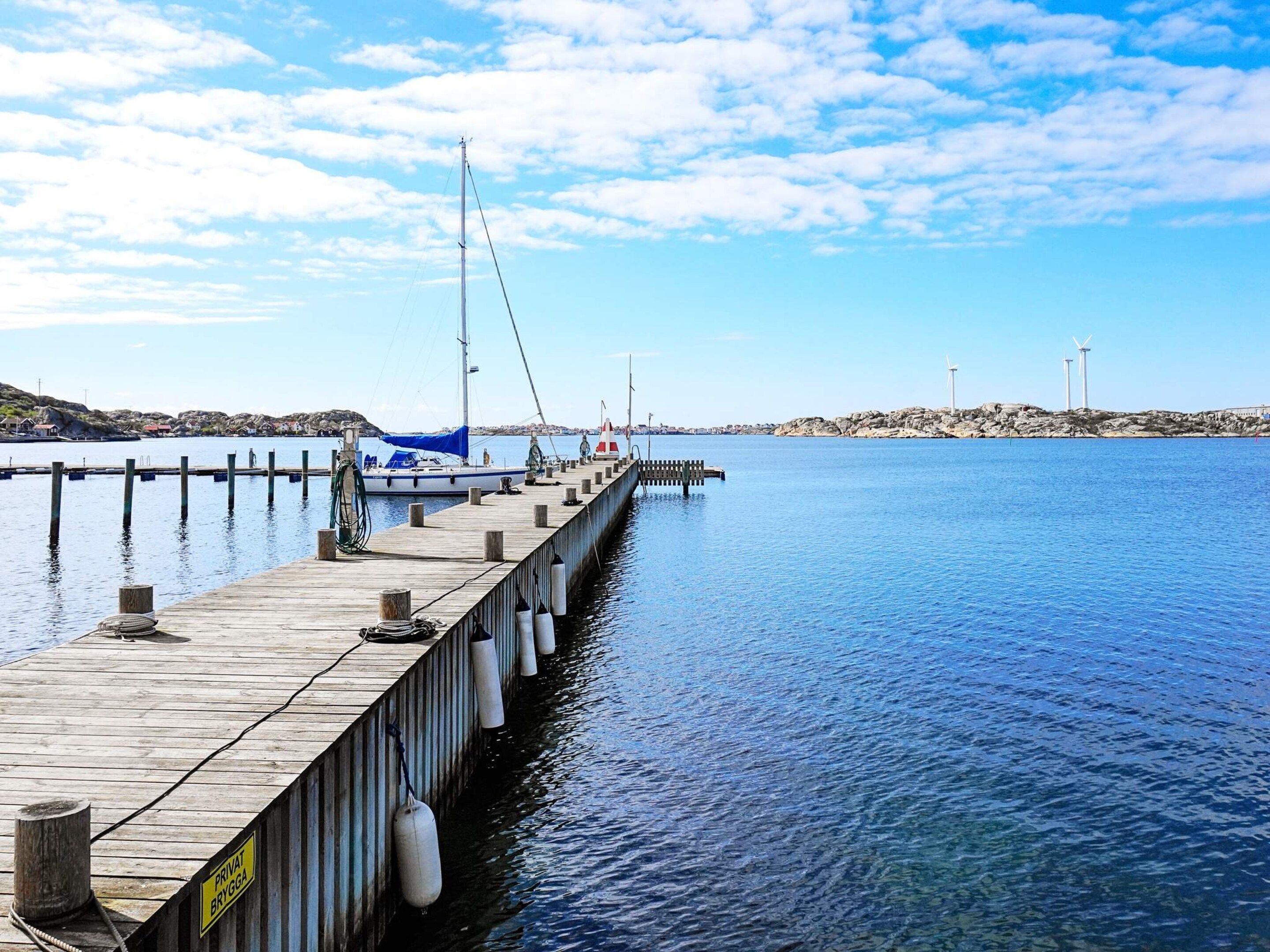 A wooden pier extending into calm water with a sailboat docked at the end.
