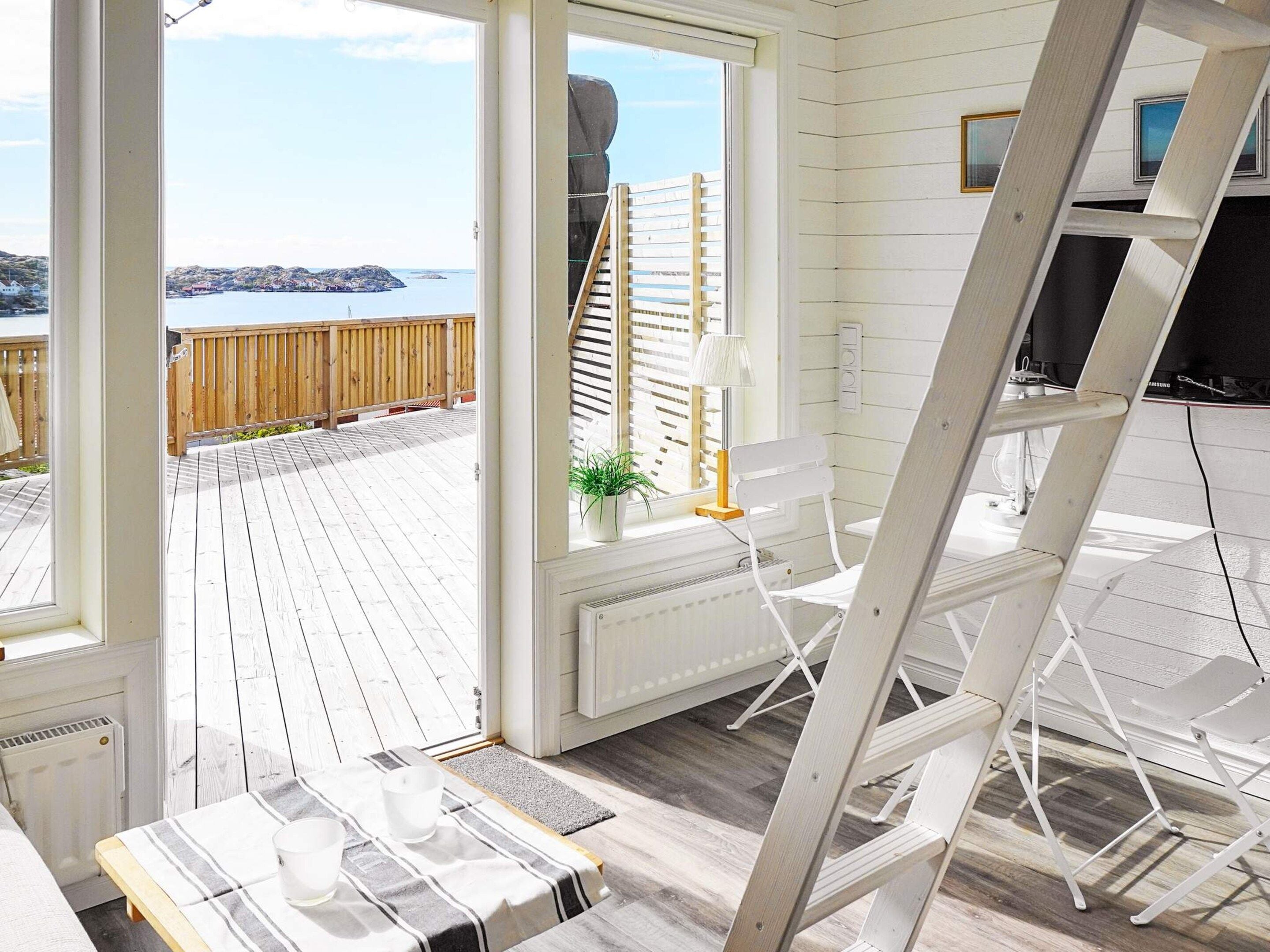 Quarto com vista para um deck de madeira e para a água, um radiador branco, uma cadeira branca e uma mesa com toalha listrada.