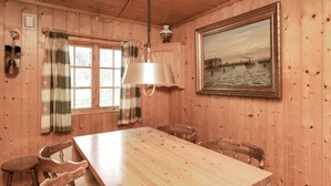 A wooden-paneled room with a large table and chairs, a hanging lamp, a painting of a river scene, and plaid curtains. - 4 Person Holiday Home in Bogo By-by Traum (Bogø By)