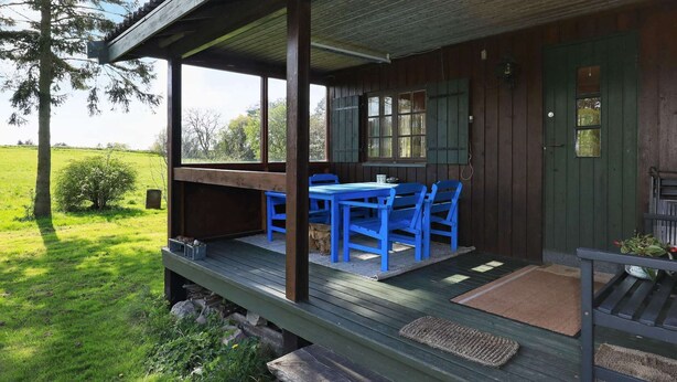 A wooden cabin with a porch, a table with blue chairs, and a green door. - 4 Person Holiday Home in Bogo By-by Traum (Bogø By)