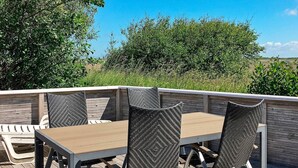 Un'area pranzo all'aperto con un tavolo di legno e quattro sedie, circondata da un pontile in legno e vegetazione.
