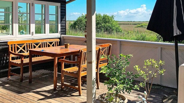 Un terrazzo in legno con tavolo e sedie, una pianta in vaso e vista sulla campagna.