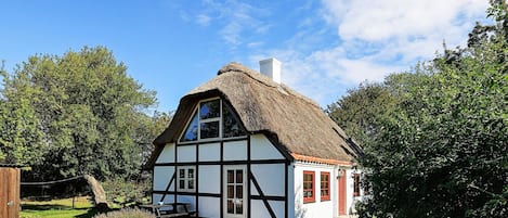Ein traditionelles Haus mit einem Reetdach und weiß-schwarzen Fassade, umgeben von viel Grün.