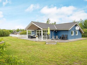 Ein blaues Haus mit überdachter Terrasse, Rasen und einer kleinen Holzterrasse.