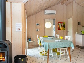 A cozy dining area with a table set for four, a wood-burning stove, and a kitchen area with a refrigerator.