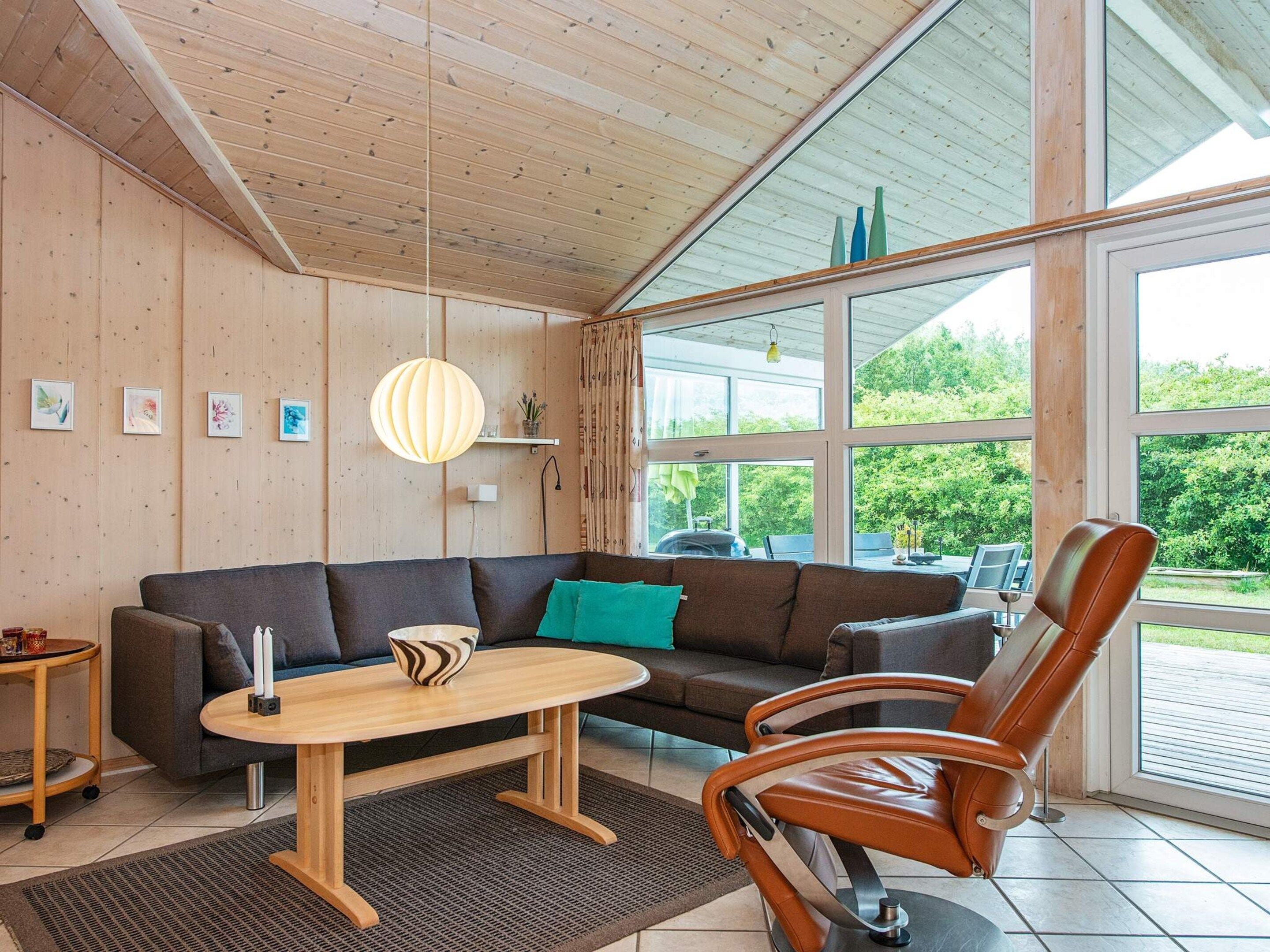 A modern living room with a wooden ceiling, a brown leather chair, a grey sofa, and a wooden coffee table.