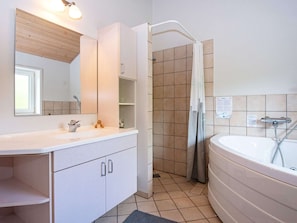 Ein modernes Badezimmer mit einer großen Badewanne, einer Dusche und einem Waschtisch mit Spiegel.