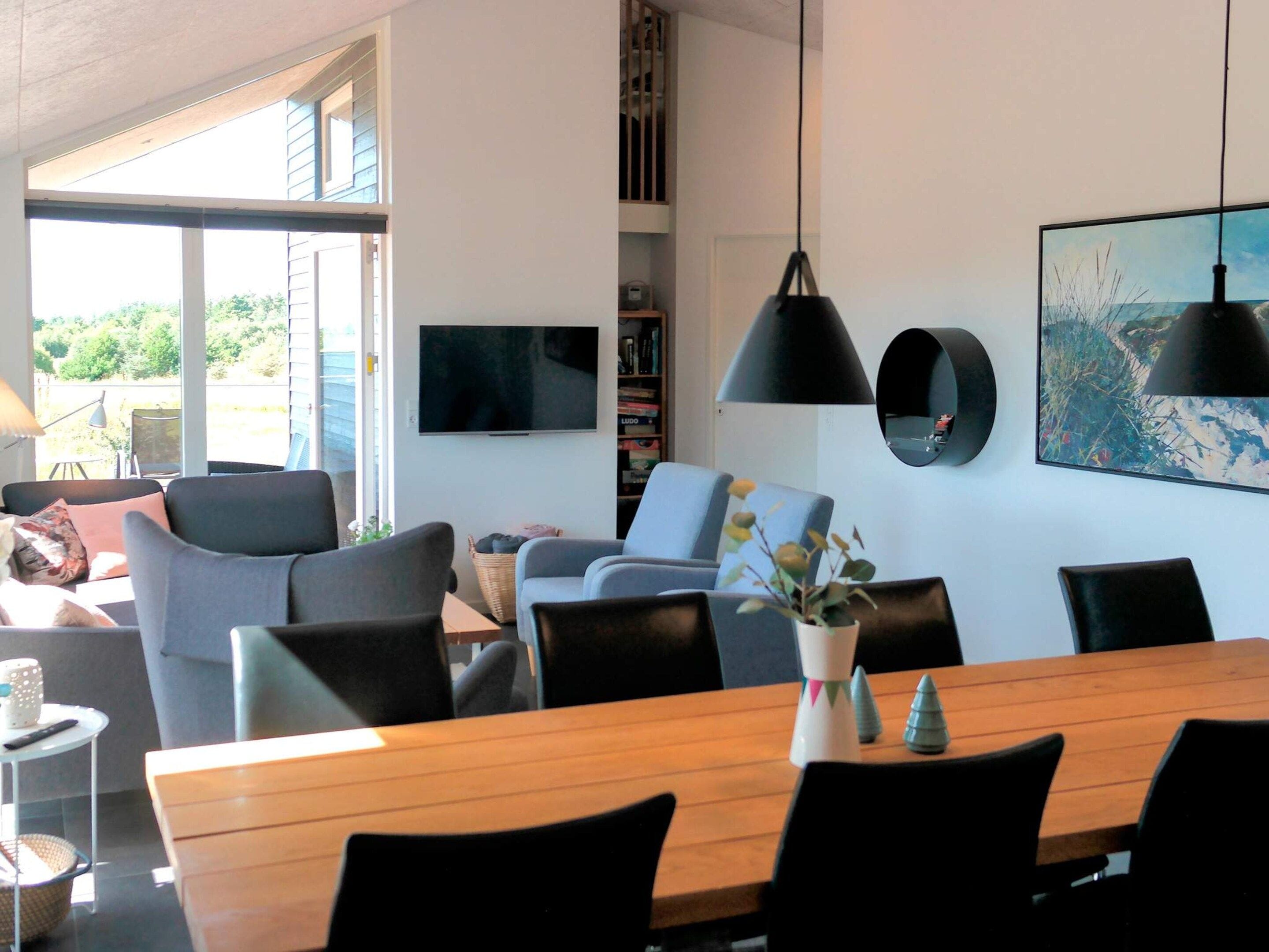 A modern living room with a wooden dining table, comfortable seating, a television, and a bookshelf.