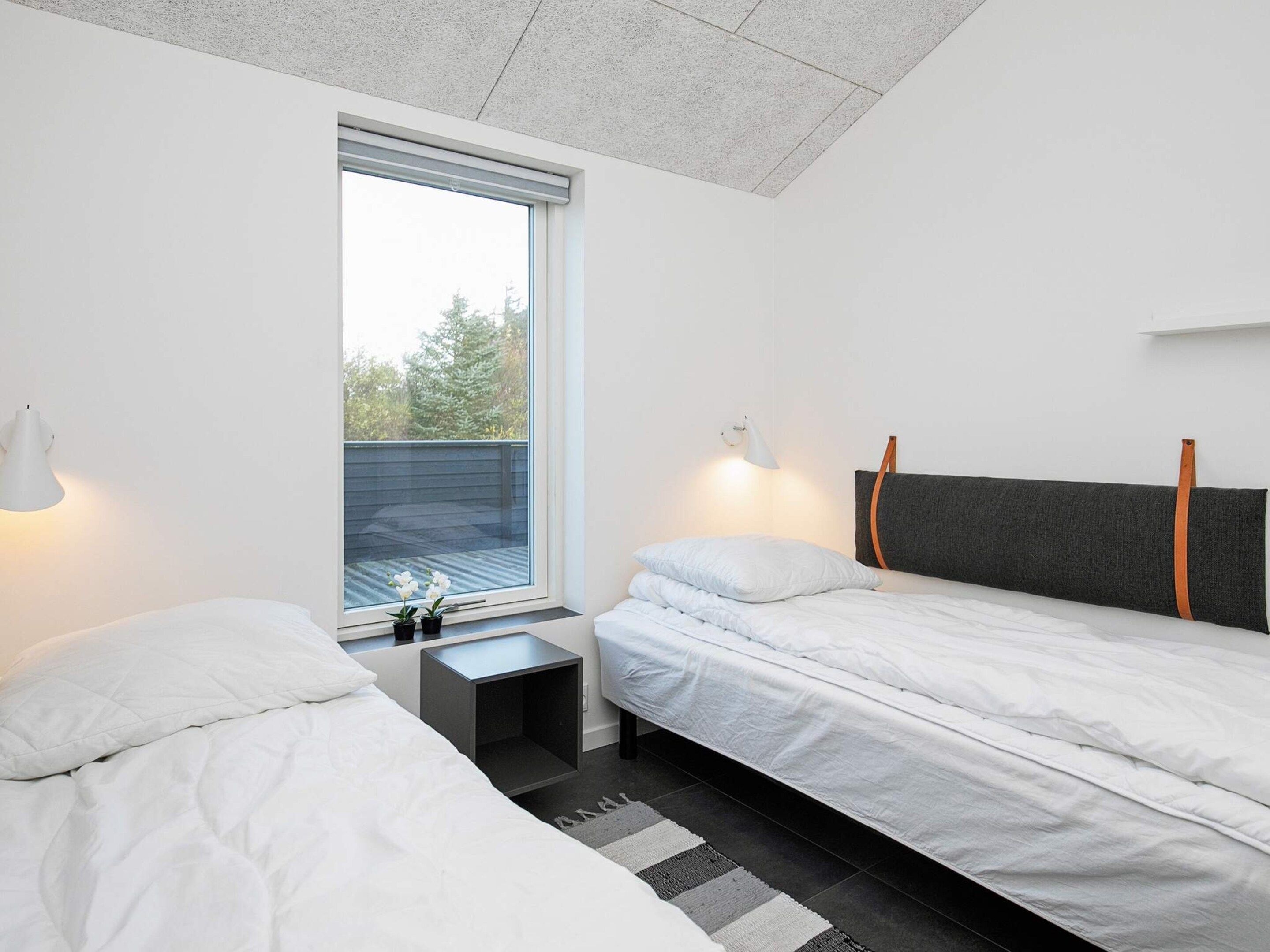 A modern bedroom with two beds, a window, and a small bedside table.