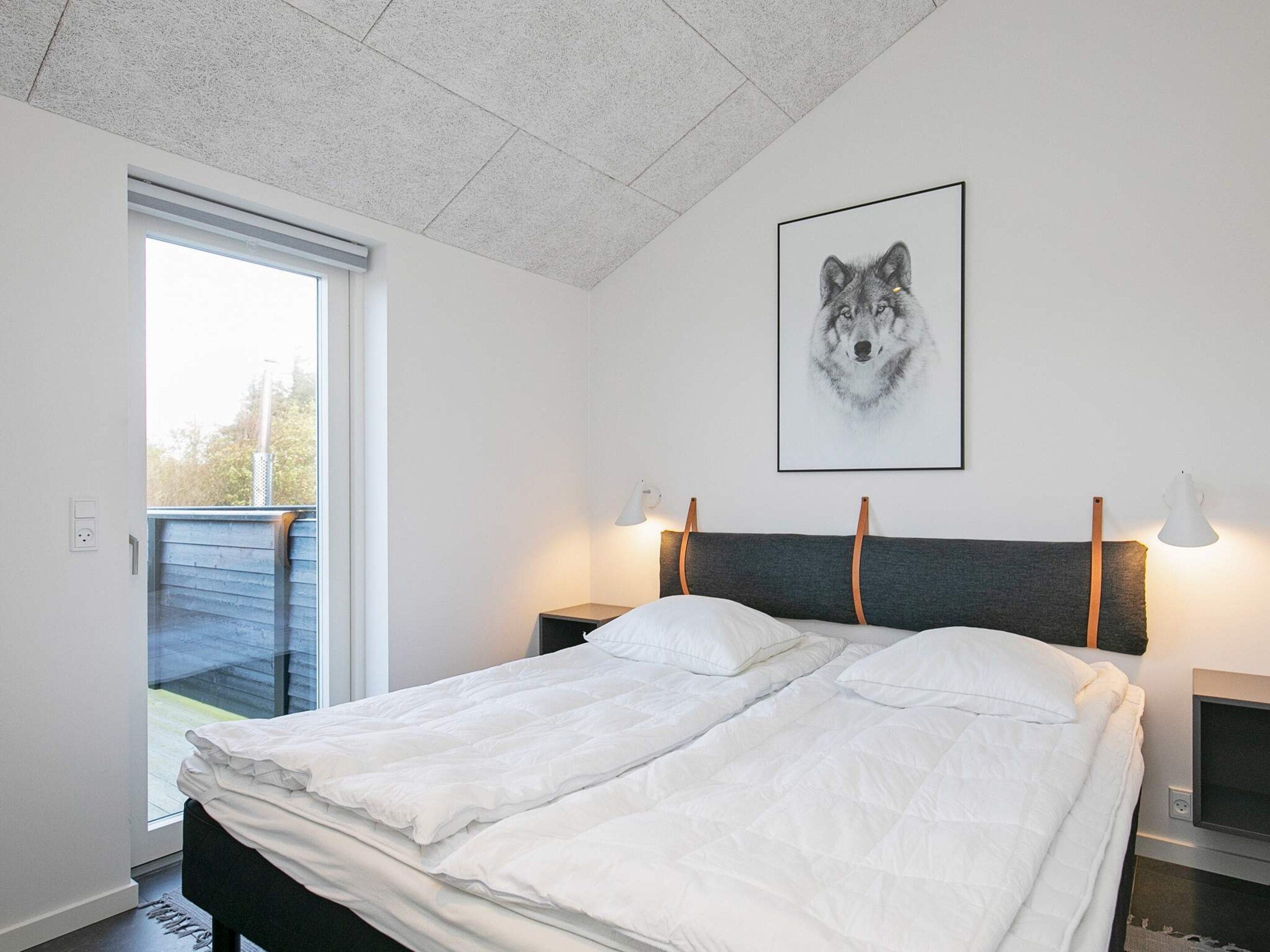 A bedroom with a bed, a window, a wall-mounted picture, bedside lamps, and a TV.