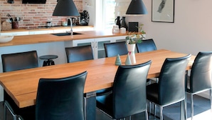 Uma cozinha moderna com parede de tijolos, luminárias pendentes pretas, mesa de jantar de madeira e cadeiras pretas.