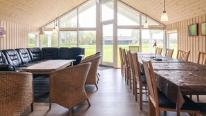 A spacious room with a large wooden ceiling, a black leather sectional sofa, wicker chairs, a wooden dining table, and large windows offering a view of the outdoors. - 4 Star Holiday Home in Idestrup (Idestrup)