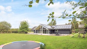 A house with a large glass door, a trampoline in the yard, and a wooden play structure. - 4 Star Holiday Home in Idestrup (Idestrup)