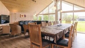 A spacious room with a large wooden table, multiple chairs, a sofa, and a television. - 4 Star Holiday Home in Idestrup (Idestrup)
