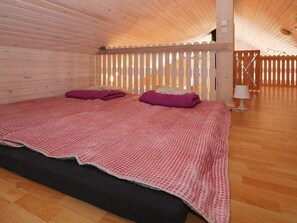A wooden cabin room with a bed, a wooden floor, and a white fence.